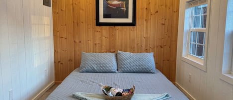 A bedroom with a bed, a chandelier, a framed picture on the wall, and a window.