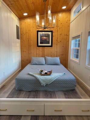 A bedroom with a bed, a chandelier, a framed picture on the wall, and a window. - Liberty-Cabin-2 @ Eagle Hollow (goreville)