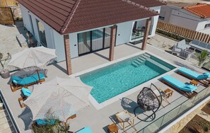 En moderne bygning med swimmingpool, liggestole og parasoller.