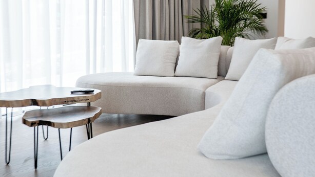 A modern living room with a curved sofa, a coffee table, and a plant. - Villa Epic (Sarande)