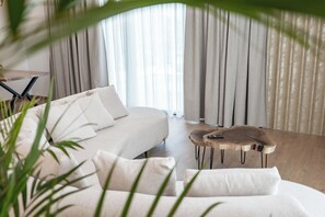 A modern living room with a sofa, a coffee table, and a view through sheer curtains.