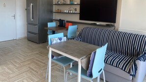Ein kompakter Wohnbereich mit Küchenzeile, Essbereich und einer Sitzecke mit Sofa und Wandfernseher.