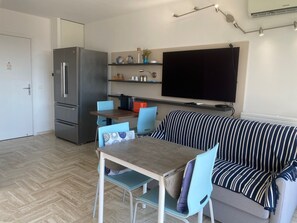 A compact living space with a kitchenette, a dining area, and a seating area with a sofa and a TV mounted on the wall. - Cannes Marina Studio with Harbor View, Pool (Mandelieu-la-Napoule)