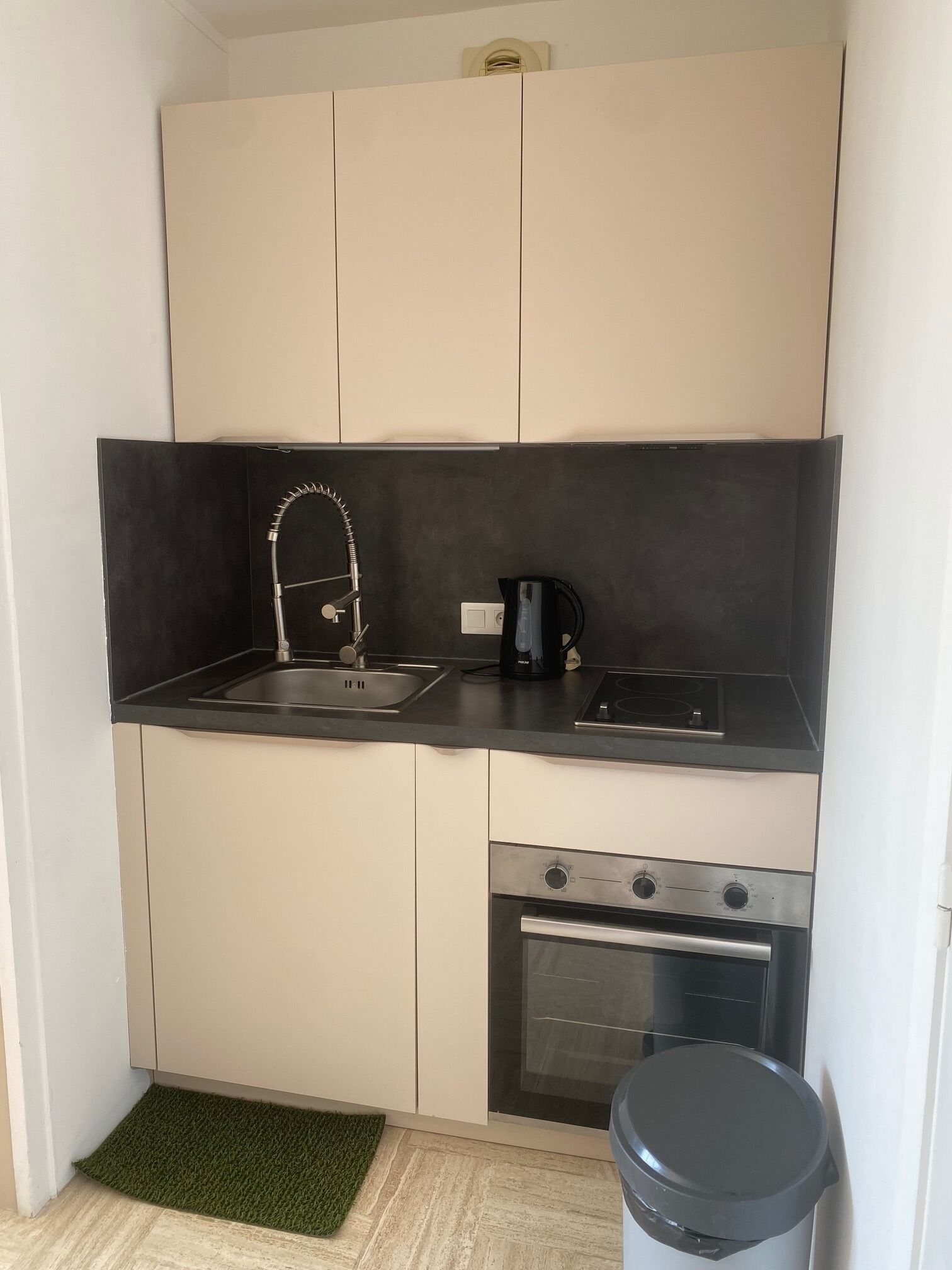 A compact kitchen with a sink, a coffee maker, a stove, and a trash bin.