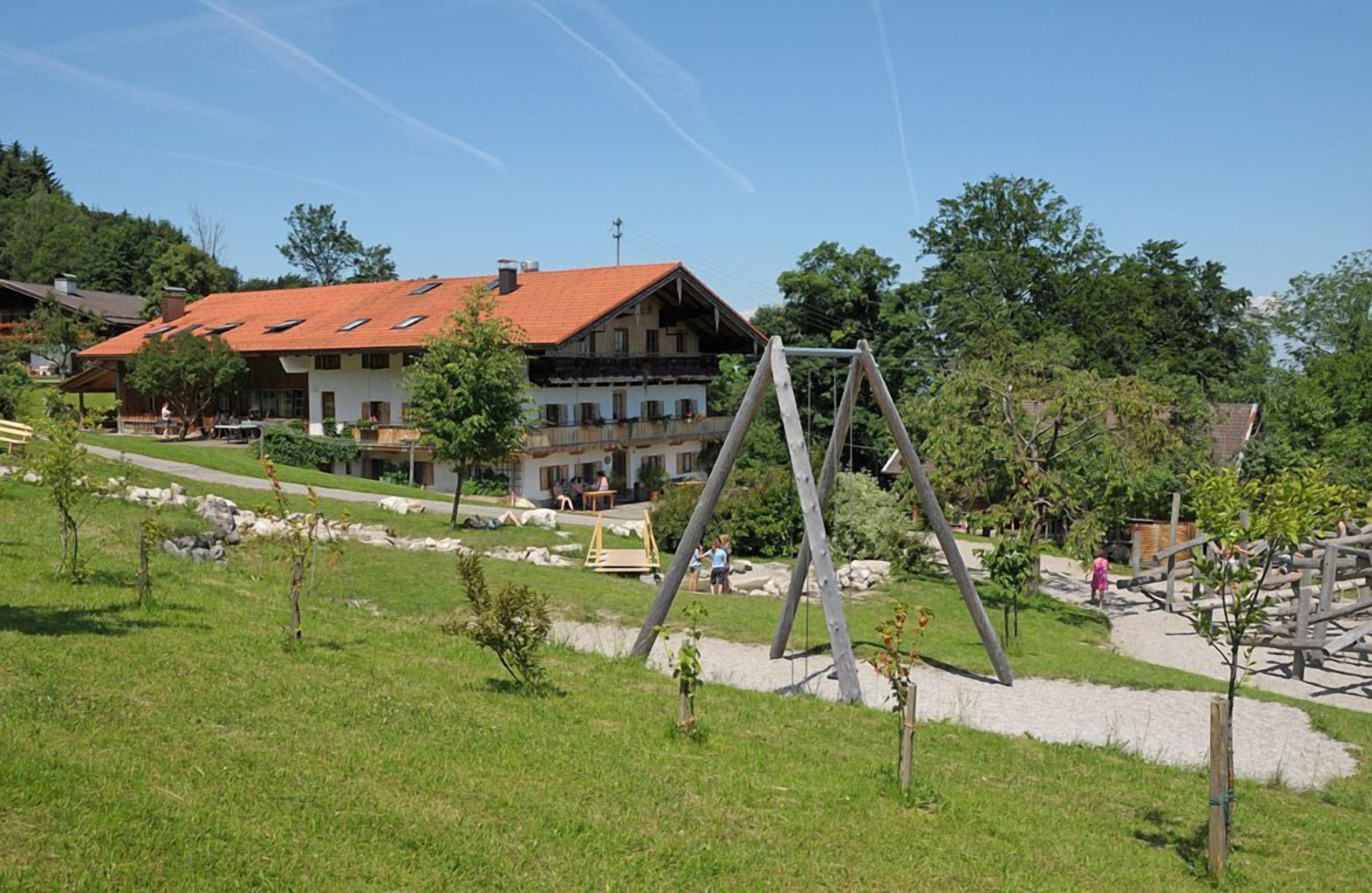 Ein Gebäude mit rotem Ziegeldach, umgeben von einer Rasenfläche mit Bäumen und einer Schaukel.