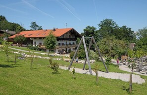 Um edifício com telhado de telhas vermelhas, cercado por uma área gramada com árvores e balanço.
