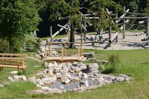 Ein Spielplatz mit Holzkonstruktionen, einer Bank und einem kleinen Teich mit Steinen.