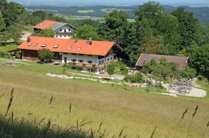 Ein Landhaus mit rotem Dach, umgeben von einer Wiese und Bäumen.