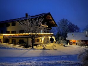 Paisagem coberta de neve com um edifício de telhado inclinado e varanda decorada com luzes.