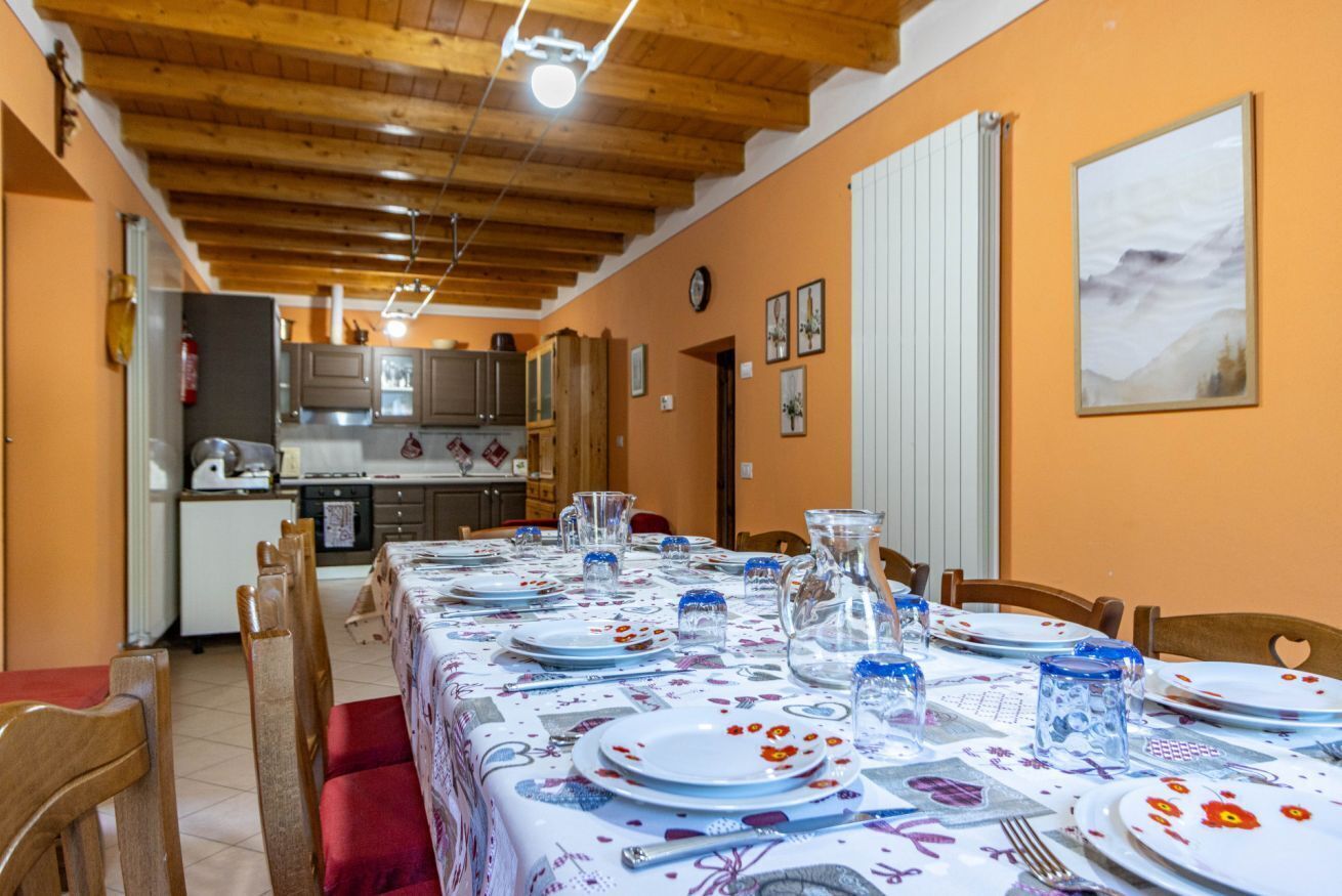 Een eetgedeelte met een tafel voor vier personen, houten stoelen, een keuken op de achtergrond en een klok aan de muur.