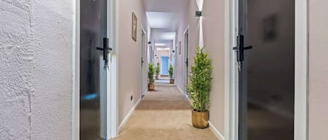 Un pasillo de hotel con pisos alfombrados, puertas a ambos lados y plantas en macetas.