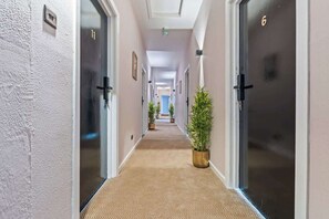 A hotel corridor with carpeted flooring, doors on both sides, and potted plants. - Stylish Double Bed Studio + Parking | Coventry CV2 (Coventry)