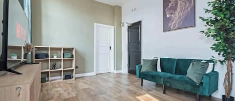 A living room with a green sofa, wooden flooring, a white door, and a plant.