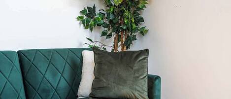 Un sofá verde con un cojín y una planta en maceta frente a una pared.