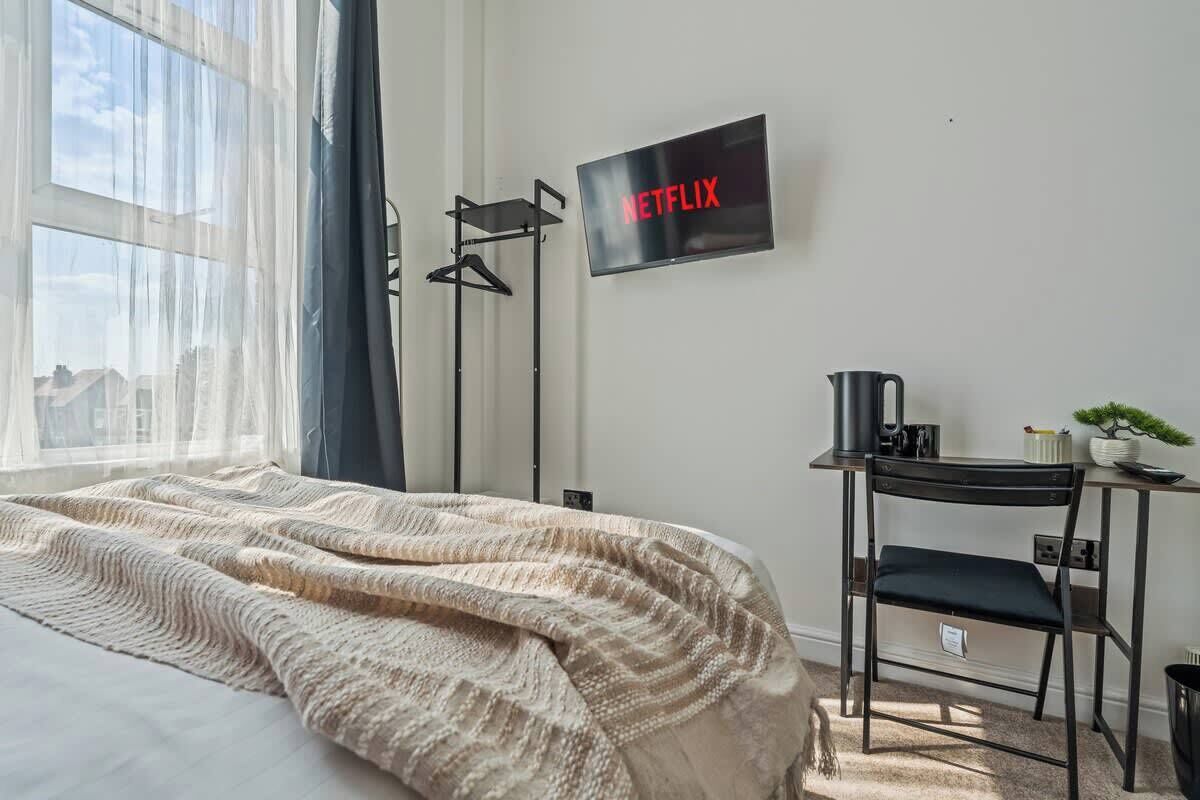 Una camera da letto con un letto, una scrivania con una sedia, una televisione e una finestra con tende.