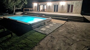 Una casa con piscina por la noche, rodeada de un jardín ajardinado.