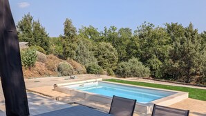 Una terraza al aire libre con piscina, rodeada de árboles y un césped bien cuidado.