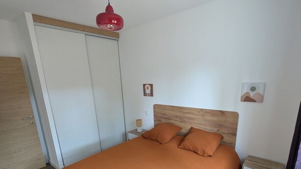 Un dormitorio con cama, armario, mesita de noche y una lámpara colgante roja.