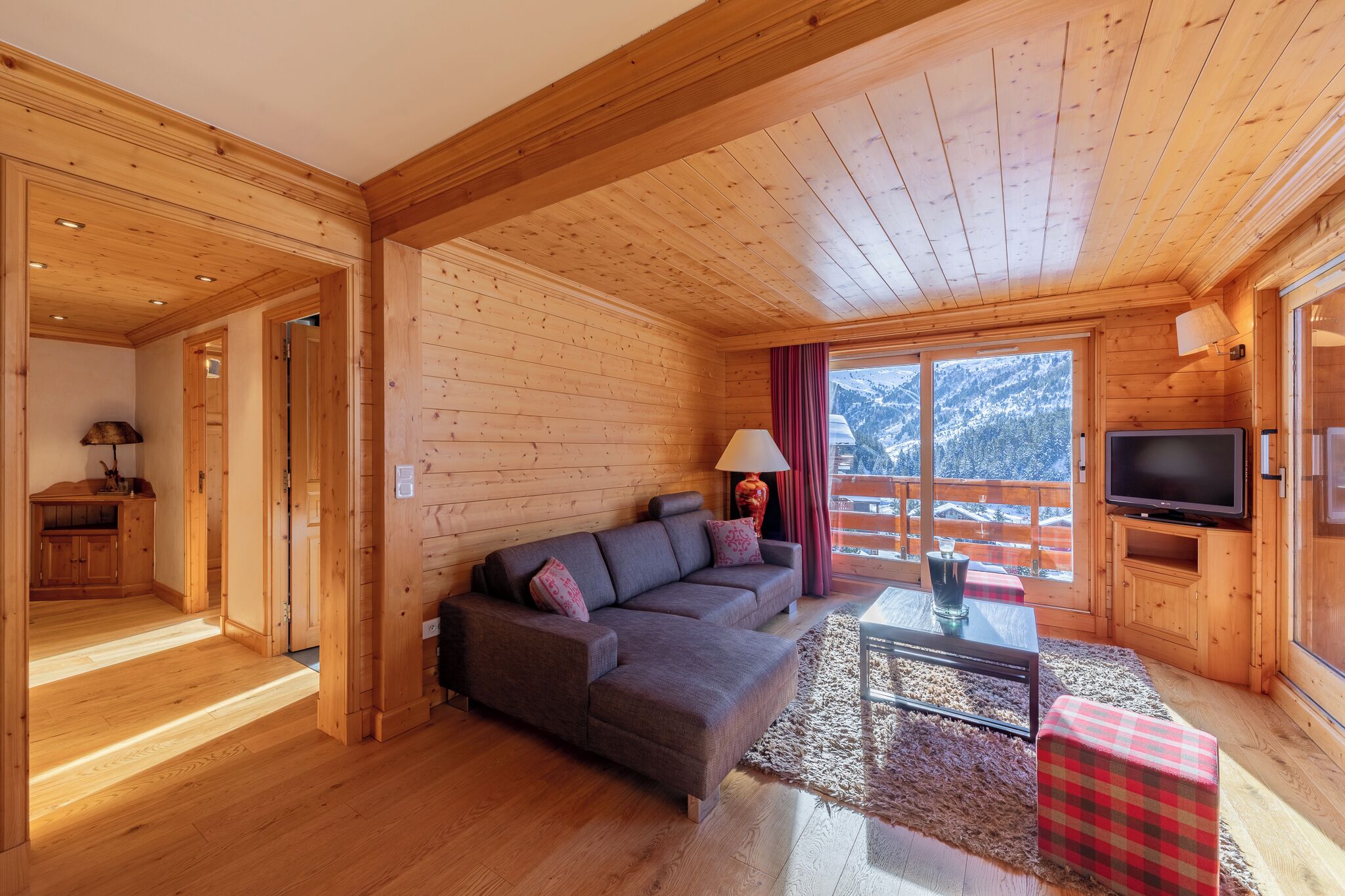 A wooden cabin interior with a sofa, TV, and a view of mountains.