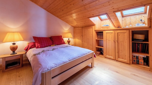Une chambre à coucher en bois, avec un lit, deux tables de chevet, une bibliothèque et des fenêtres de toit.