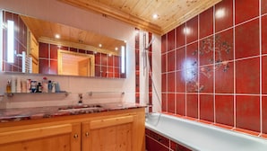 Une salle de bain avec un meuble-lavabo en bois, un grand miroir, une baignoire aux carreaux rouges et une douche.