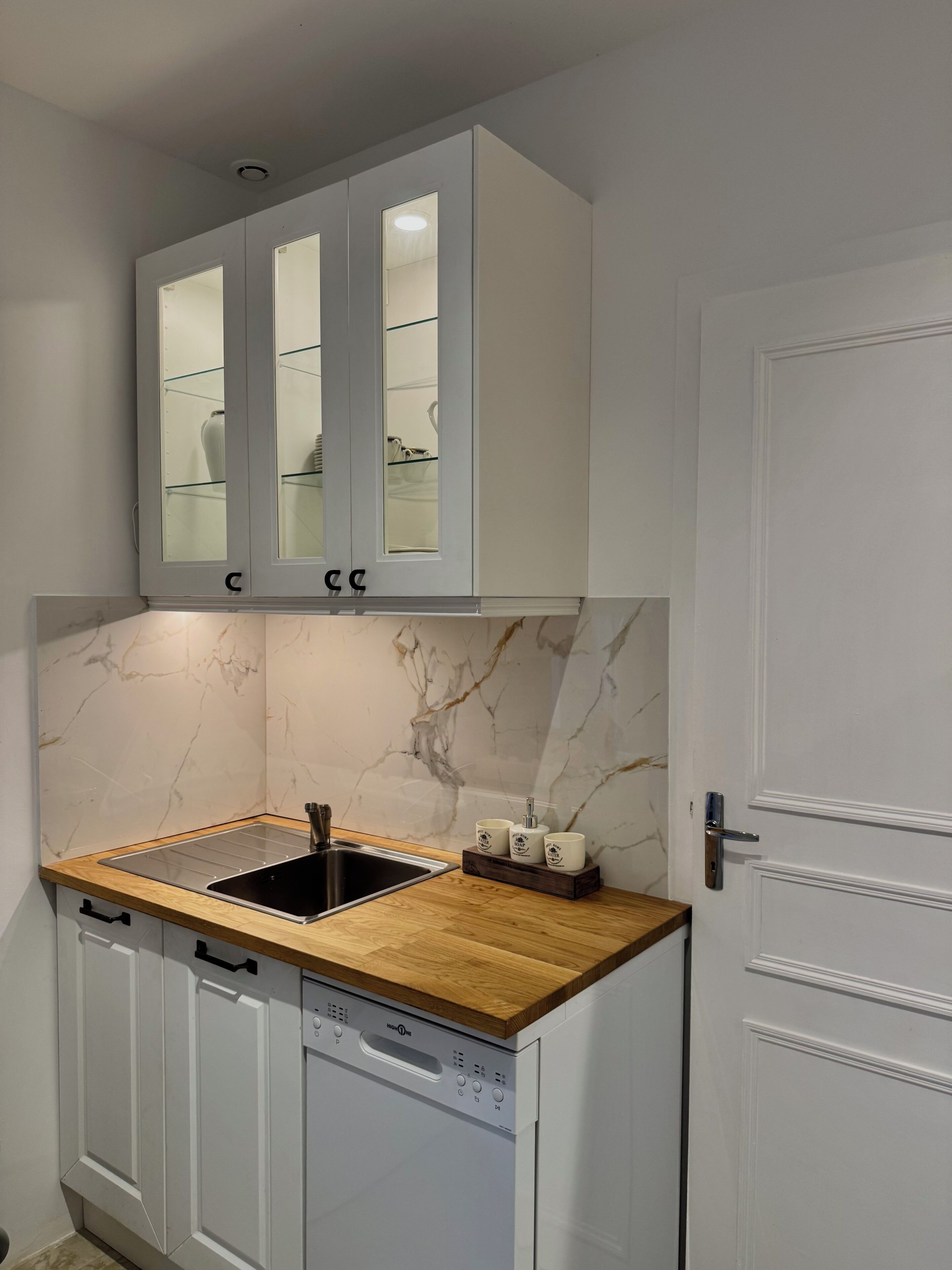 A compact kitchen with a built-in dishwasher, a wooden countertop, and a white door.