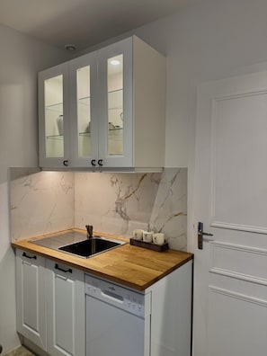 A compact kitchen with a built-in dishwasher, a wooden countertop, and a white door. - Luxury Studio Apartment in the Morvan Regional Park (Saint-Honoré-les-Bains)