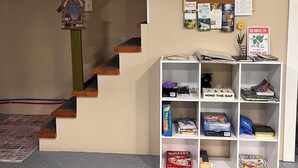 Eine Treppe mit Holzgeländer, ein Schwarzes Brett mit verschiedenen Aushängen und eine weiße Regaleinheit mit Büchern und Spielen.