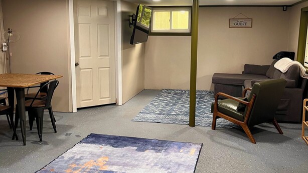 Une pièce comprenant une table à manger, des chaises, un canapé, un téléviseur fixé au mur et un tapis sur le sol.