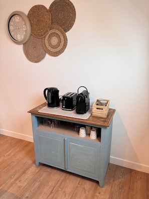Une petite cuisine équipée d’une horloge, d’une décoration murale en fibres tressées et d’un coin café.