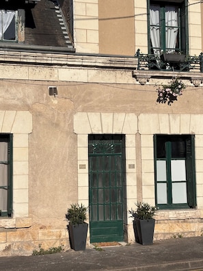 A building facade with a green door, two potted plants, and a window with a curtain.