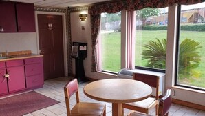 Una cocina con una mesa y sillas, una ventana con vista a un área verde, y una puerta con un letrero.