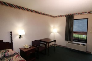 Habitación de hotel con cama, escritorio, silla, teléfono, lámpara y ventana con vistas.