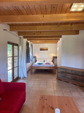 A room with a wooden ceiling, a bed with floral bedding, a red sofa, and a wooden bench. - Waldrausch Vacation Home (Siegsdorf-Vorauf)