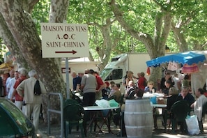 Une enseigne indiquant « MAISON DES VINS A.O.C SAINT-CHINIAN », avec une foule de personnes et des tables à l'extérieur.