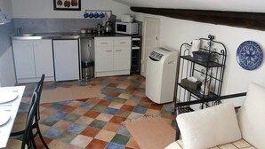 A compact kitchen with white cabinets, a microwave, and a sink. There is a dining table with chairs and a sofa with cushions. The floor has a checkered pattern. - Spacious loft apartment in charming Saint-Chinian (saint-Chinian)