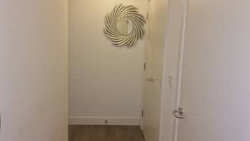A hallway with a wooden floor, a white door, and a wall-mounted light fixture.