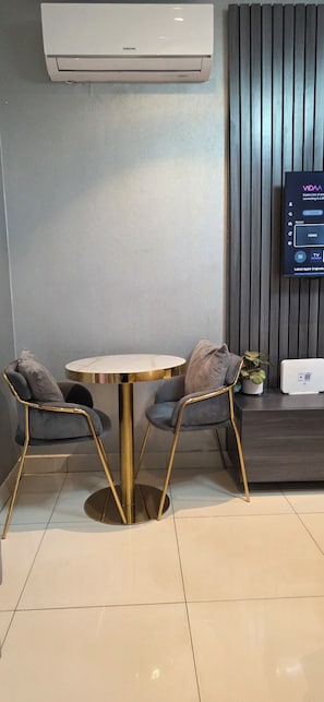 A modern room with a round table, two chairs, a mounted TV, and an air conditioner. - Lennox Apartment Exquisite (Accra)