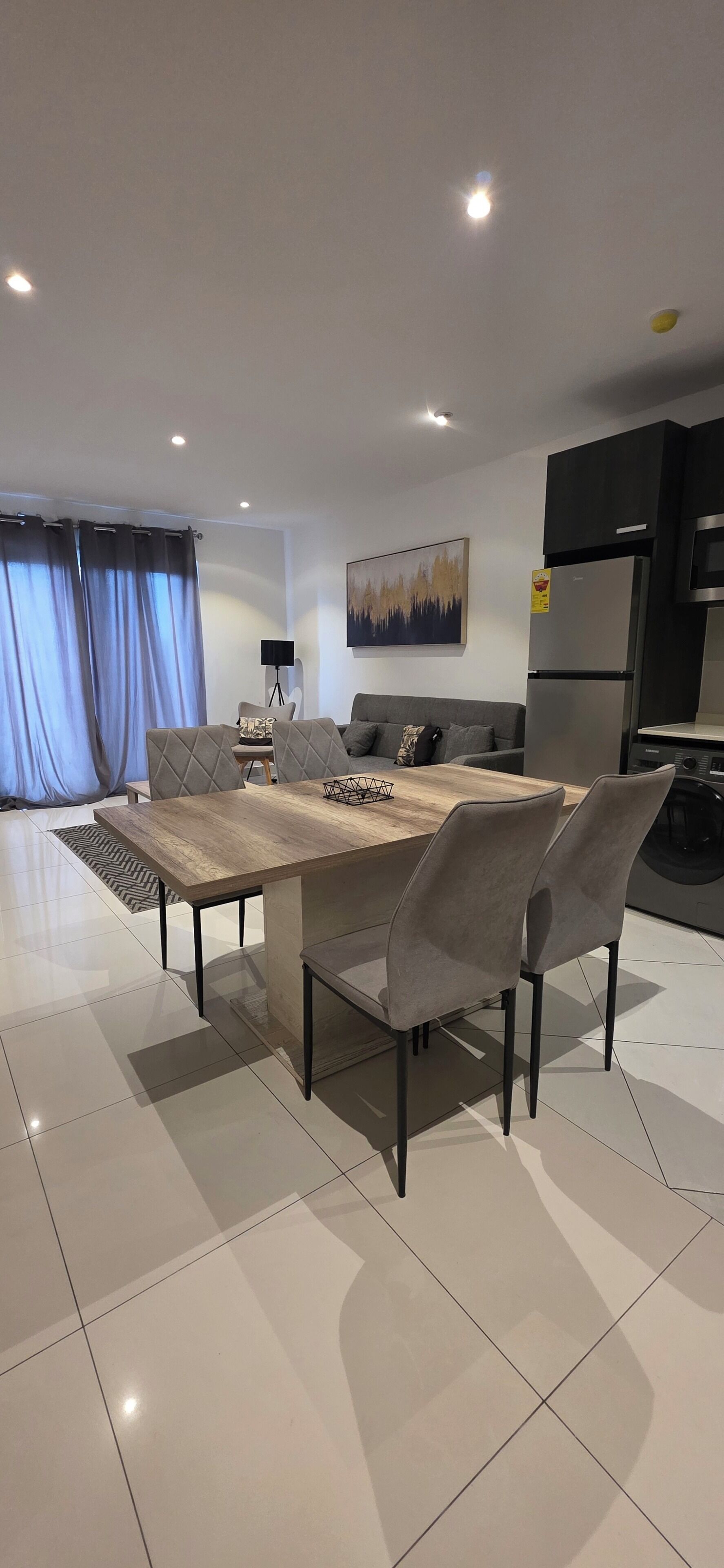 A modern living room with a dining table, grey sofas, and a flat-screen TV.
