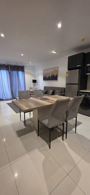 A modern living room with a dining table, grey sofas, and a flat-screen TV. - Lennox Apartment Exquisite (Accra)