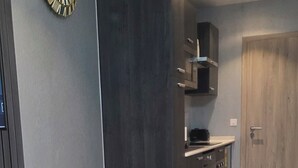 Un dormitorio moderno con cama, un armario de madera oscura, una zona de cocina integrada y un reloj montado en la pared.