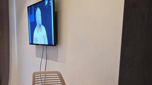 Una habitación con televisión montada en la pared, una mesita plegable y una silla.