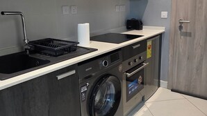 Una cocina moderna con armarios oscuros, un microondas integrado, una lavadora y un lavabo.