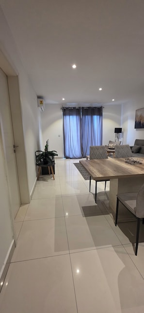 A spacious living area with a dining table, a sofa set, and a large window with curtains. - Lennox Apartment Exquisite (Accra)