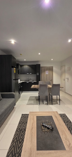 A modern living room with a sofa, a coffee table, and a dining area with chairs. - Lennox Apartment Exquisite (Accra)