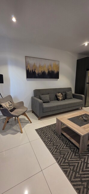 A modern living room with a grey sofa, a wooden coffee table, a patterned rug, and a wall-mounted abstract painting. - Lennox Apartment Exquisite (Accra)