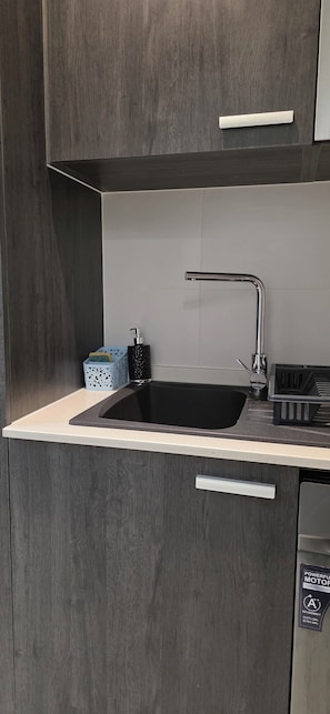 A kitchen with a black sink, stainless steel faucet, and a white countertop. - Lennox Apartment Exquisite (Accra)