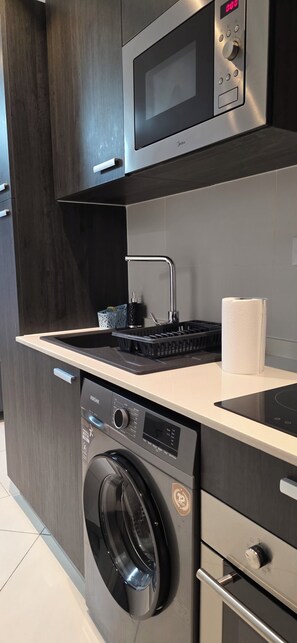 A modern kitchen with a built-in washer and dryer, a microwave, and a stainless steel range hood. - Lennox Apartment Exquisite (Accra)