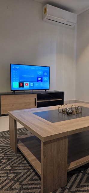 A modern living room with a flat-screen TV, wooden coffee table, and a remote holder. - Lennox Apartment Exquisite (Accra)