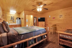 A wooden cabin interior with a bed, a television, a refrigerator, and a kitchen area. - Pet Friendly Cabin in Gatlinburg (Gatlinburg)